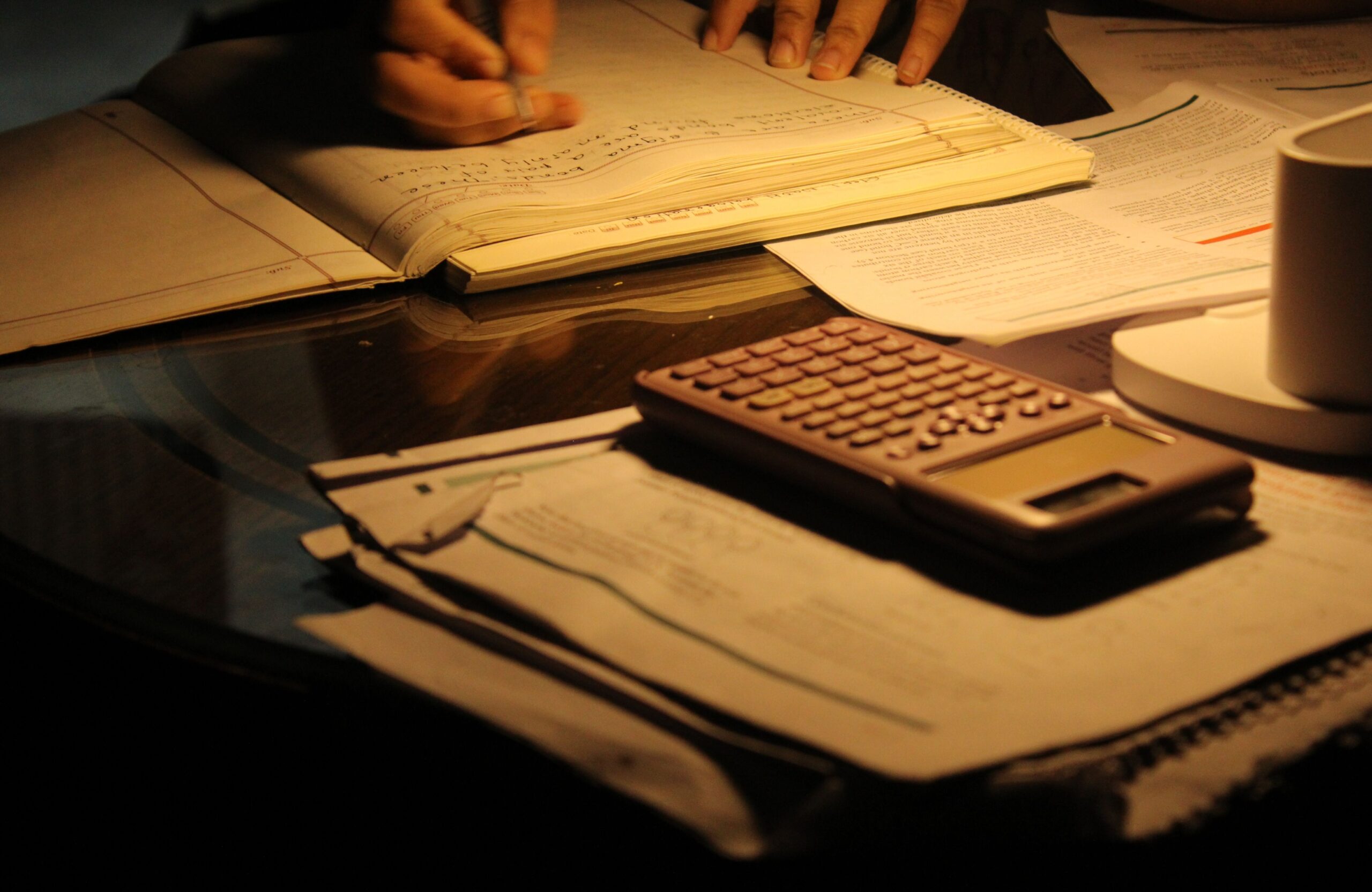夜に電卓とノートを使って資格の勉強をする様子