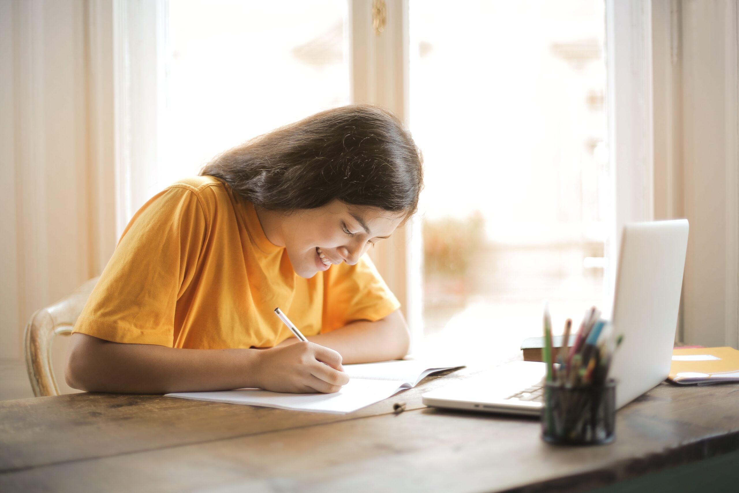 自宅のノートパソコンとノートで英語学習をする女性